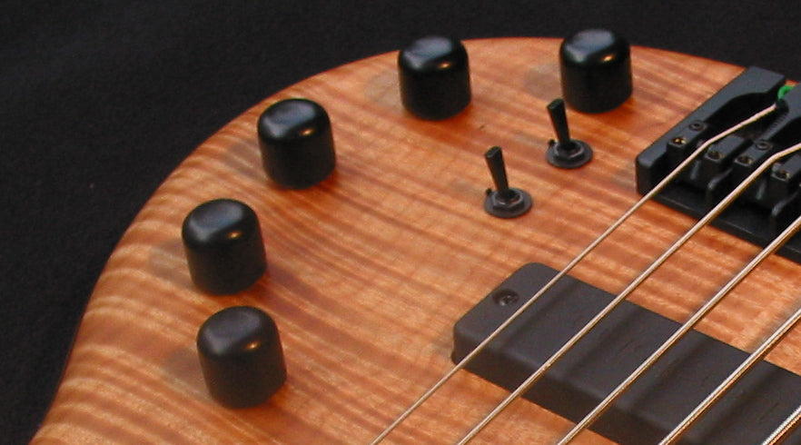 Featured image for Bass Preamps showing a 4 string maple topped bass with the knobs and switches indicating a bass preamp inside