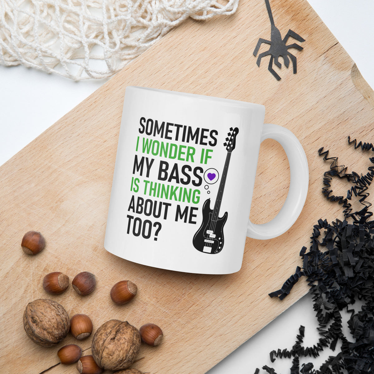 White mug with a guitar graphic and text on a wooden board with nuts and decorative items.